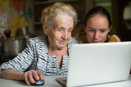 An older person using a laptop to browser the Internet, with the help of a younger person